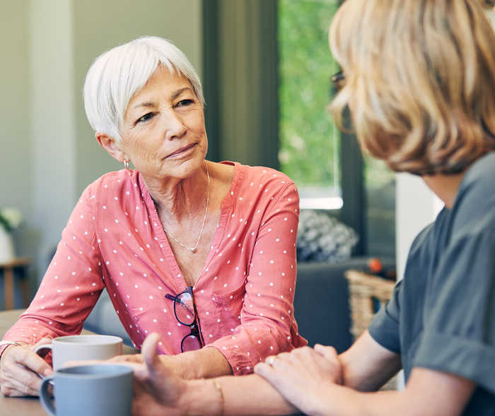 Zwei Frauen sitzen sich gegenüber und halten Tassen in den Händen.
