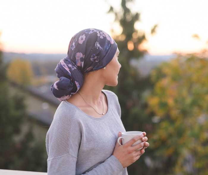  Une femme portant un foulard et une tasse dans les deux mains regarde par-dessus son épaule gauche.