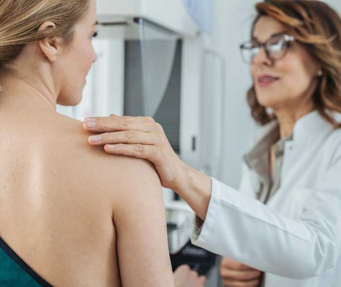 Une médecin pose sa main sur l’épaule dénudée d’une patiente.