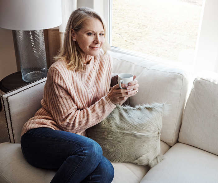 Une femme est assise sur un canapé et tient une tasse.