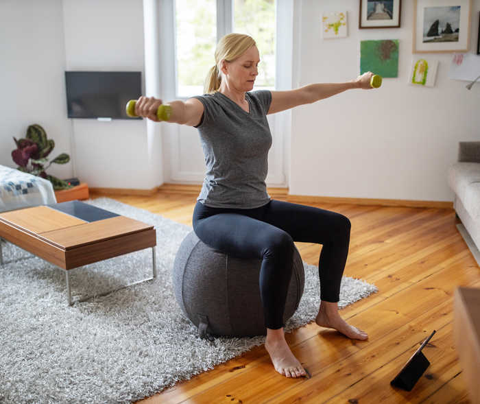 Une femme est assise sur un ballon de gymnastique et tient des haltères dans les mains.