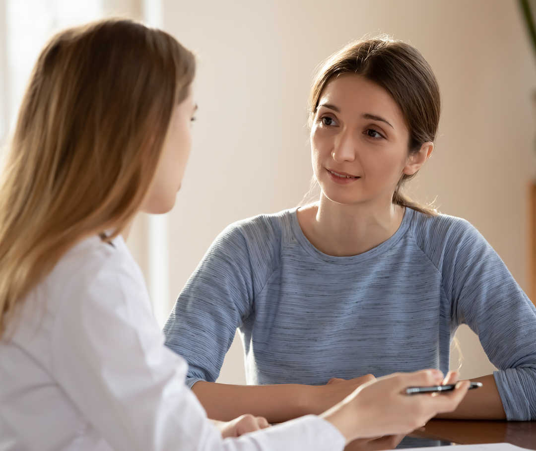 Zwei Personen unterhalten sich an einem Tisch. Eine Person trägt einen weißen Kittel.
