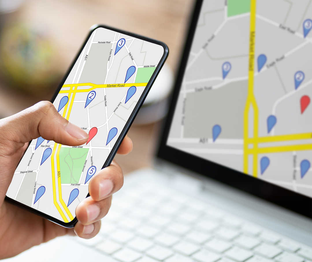 Nahaufnahme eines aufgeklappten Laptops und eines Smartphones in der Hand mit einer digitalen Karte. 