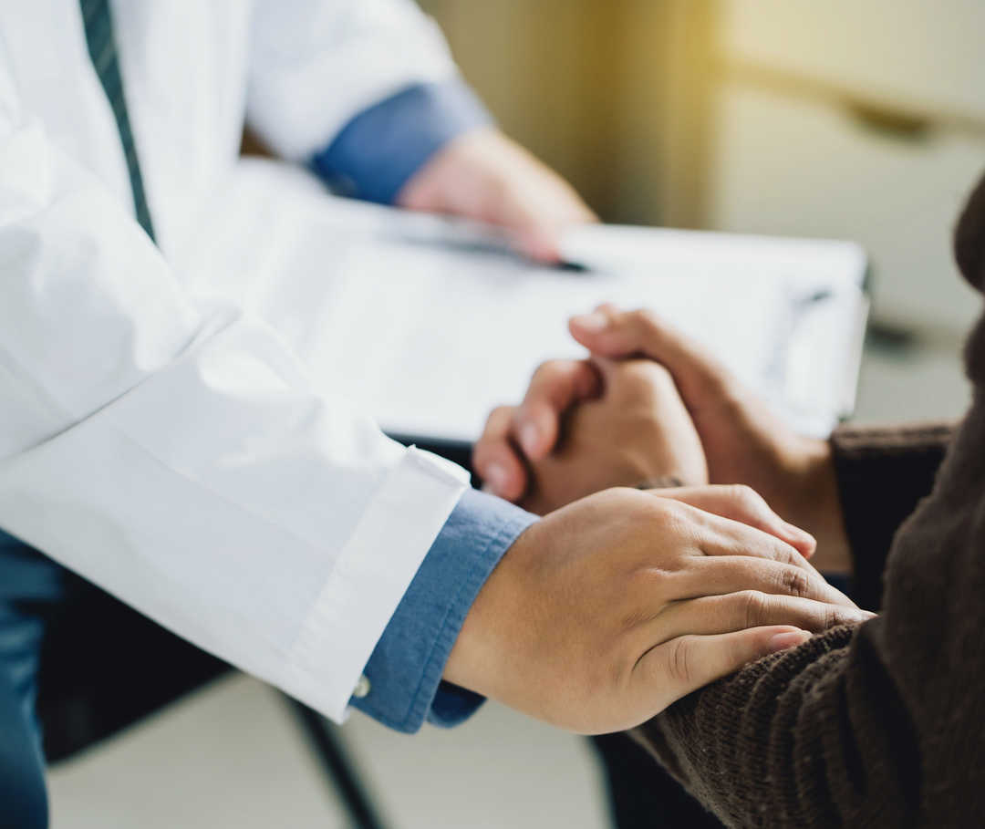 Gros plan sur une personne en blouse blanche qui touche l′avant-bras d′une autre personne.