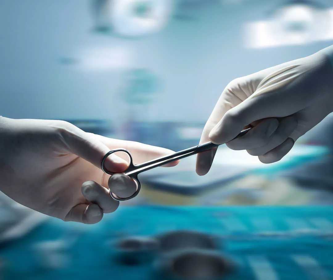 Primo piano di due mani con guanti che tengono un paio di forbici. 