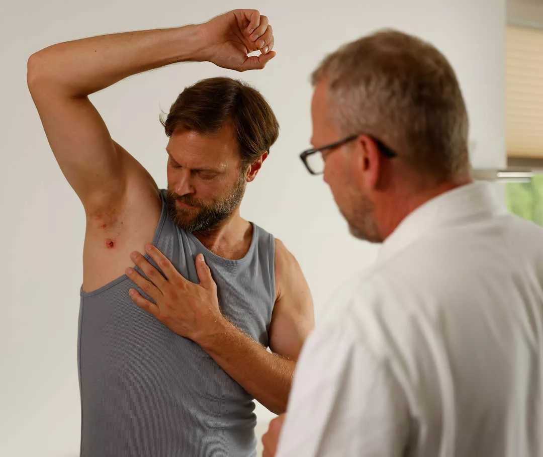 Una persona in camice bianco guarda un’altra persona che mostra l’ascella con lesioni da acne inversa. 