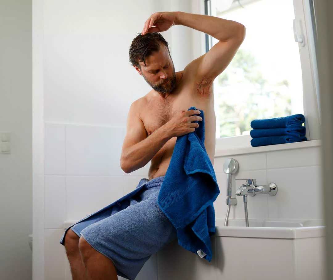 Una persona seduta sulla vasca da bagno con un’ascella ben visibile tiene in mano un asciugamano