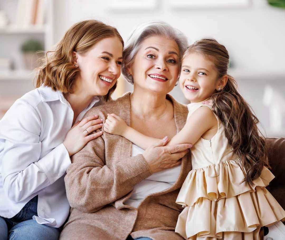 Tre soggetti femminili sorridenti di età diverse si abbracciano.