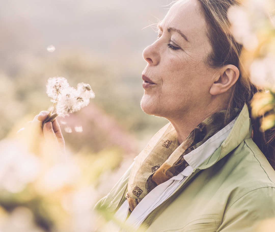 Eine Frau pustet auf einige Pusteblumen in ihrer Hand.