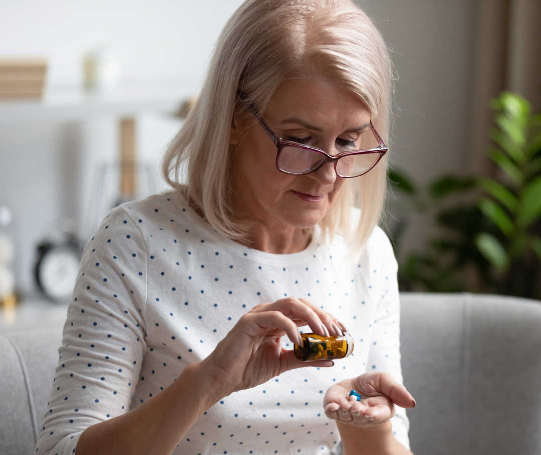 Behandlungsmöglichkeiten von Knochenmetastasen Eine Frau, die sich Tabletten in die Hand schüttet.