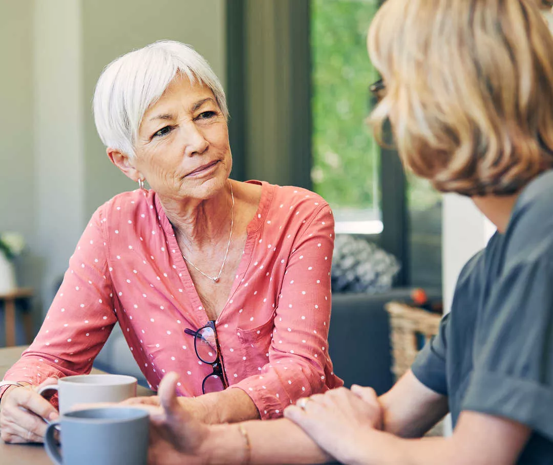 Zwei Frauen sitzen sich gegenüber und halten Tassen in den Händen.