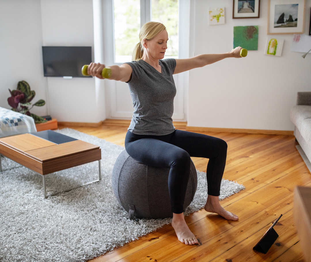 Eine Frau sitzt mit Hanteln in der Hand auf einem Gymnastikball.