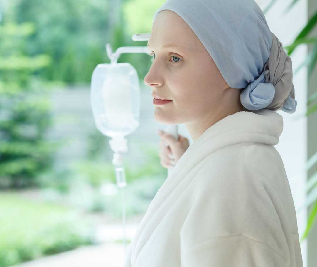 Une femme tient un support à perfusion et regarde par la fenêtre.