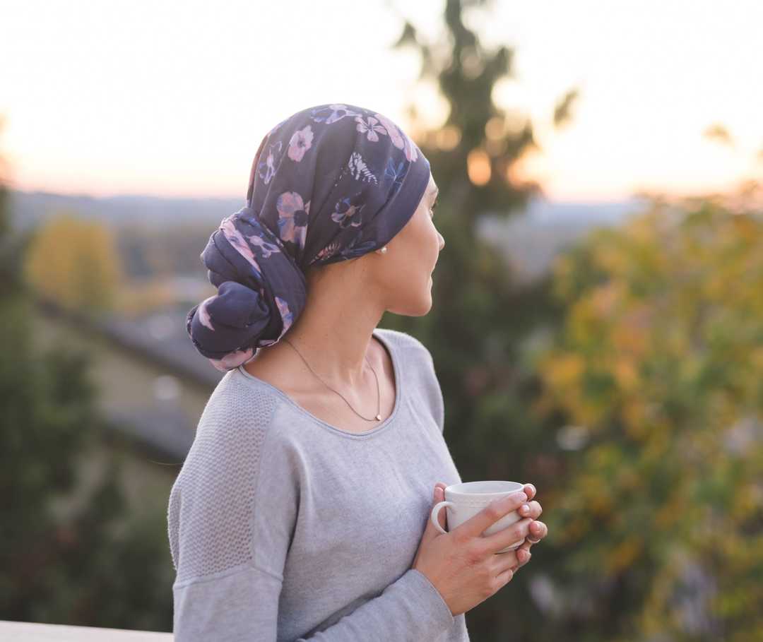  Une femme portant un foulard et une tasse dans les deux mains regarde par-dessus son épaule gauche.