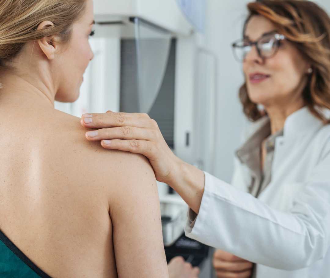 Une médecin pose sa main sur l’épaule dénudée d’une patiente.