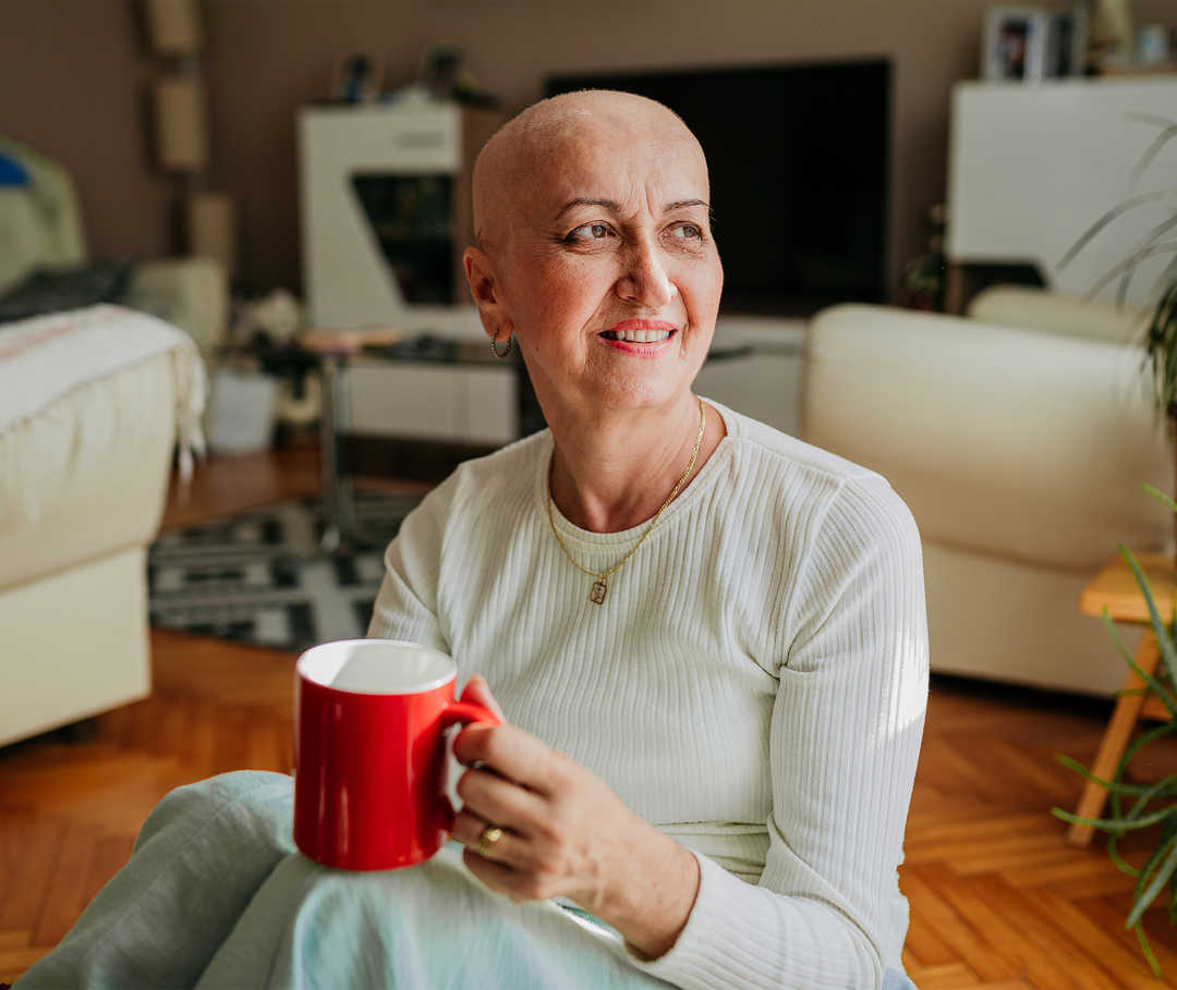 Une femme sans cheveux assise au sol tient une tasse.