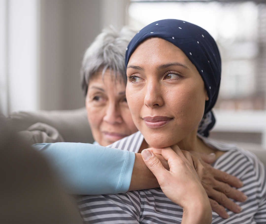 Au premier plan, une femme avec un foulard autour de la tête, enlacée par une femme plus âgée.