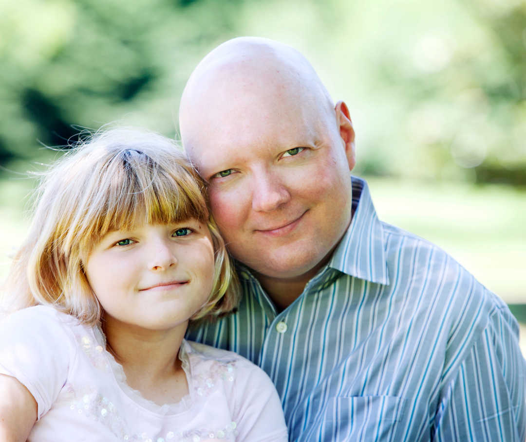 Une fille et un homme chauve sourient.