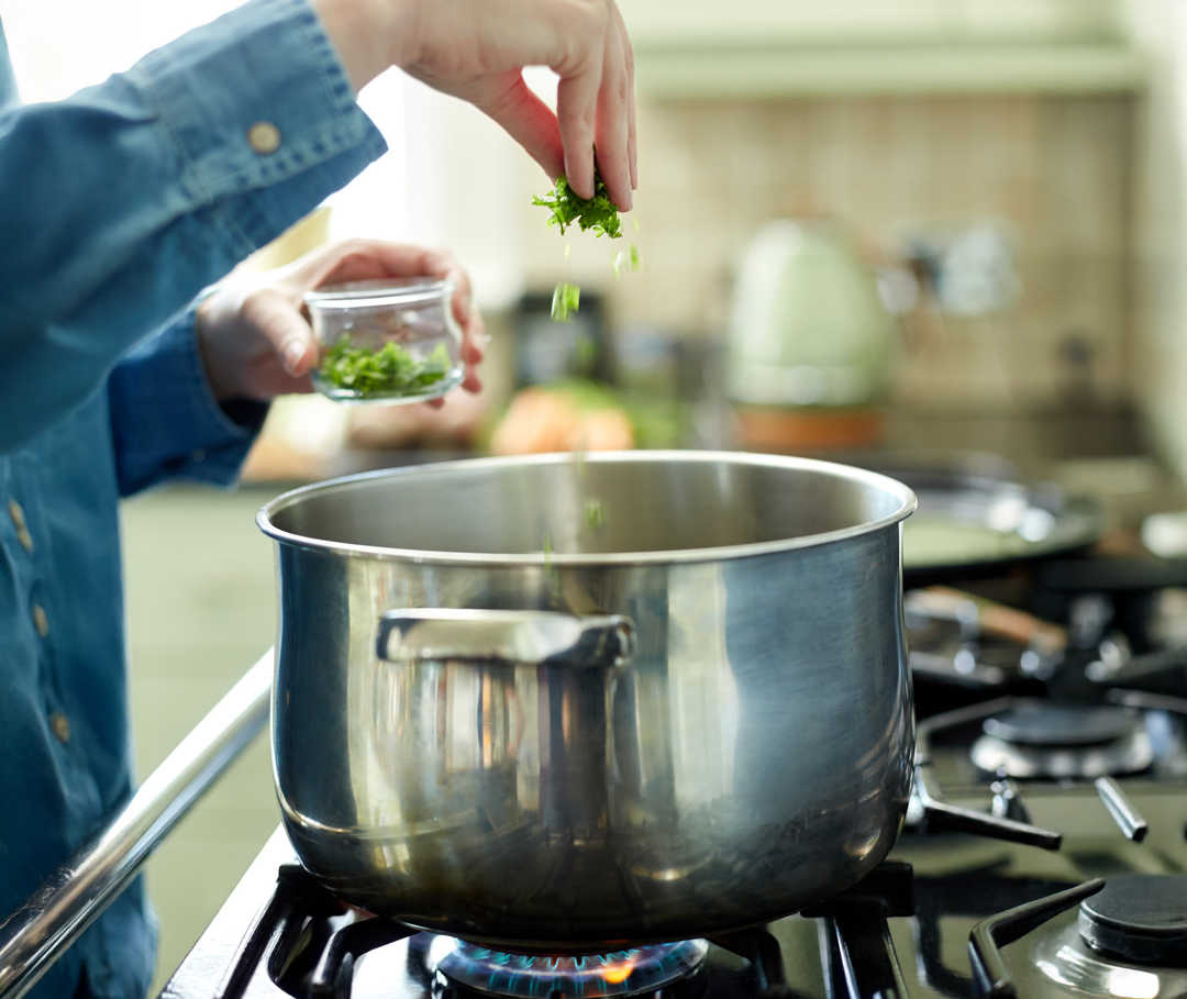 Une main fait tomber des herbes dans une casserole.